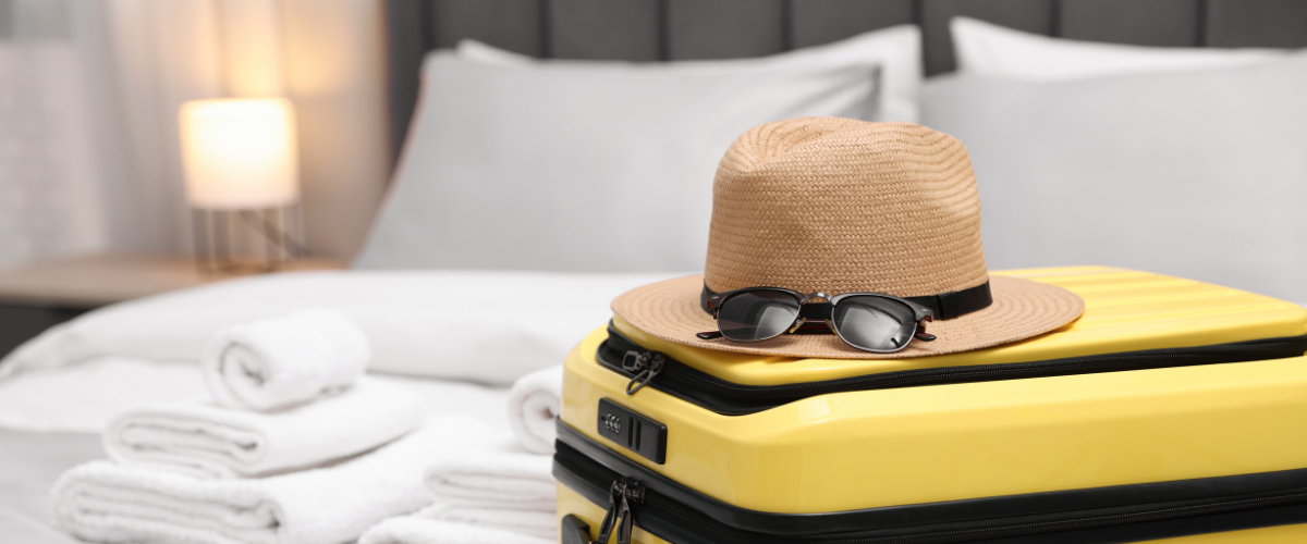 Koffer, hoed en zonnebril liggen opgestapeld op een hotelbed